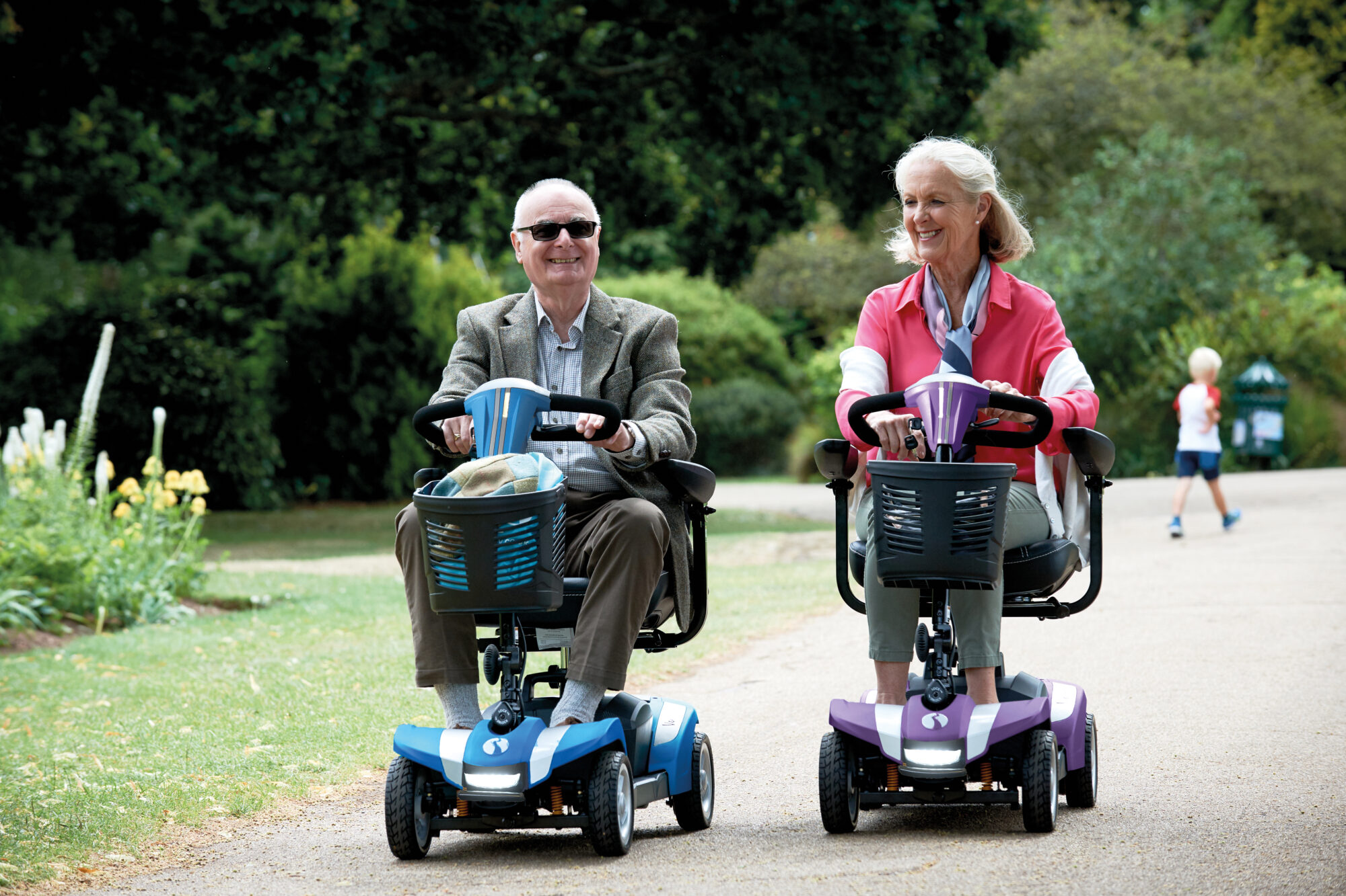 man and woman enjoying a trip through the park on their mobility scooters